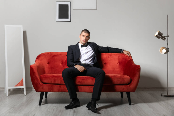 Красивий молодий чоловік в елегантному костюмі сидить на дивані в приміщенні
 - Фото, зображення