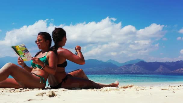 2人の女の子が楽しい時間を過ごし砂浜でパンフレットを読み - 映像、動画