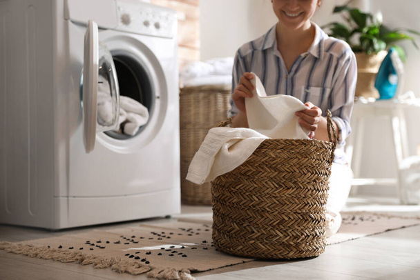 Young woman with laundry basket near washing machine at home - Foto, Imagen