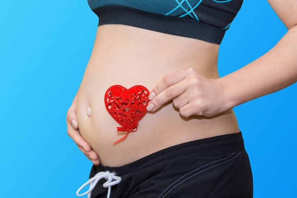 těhotenství, mateřství a mateřství koncept - šťastný budoucí matka drží červené srdce na modrém pozadí - Fotografie, Obrázek