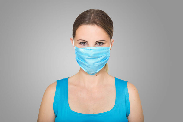 Yüz maskesi takan genç bir kadının stüdyo portresi, kameraya bakıyor, yakın plan, gri arka plan. Grip salgını, toz alerjisi, virüse karşı koruma - Fotoğraf, Görsel