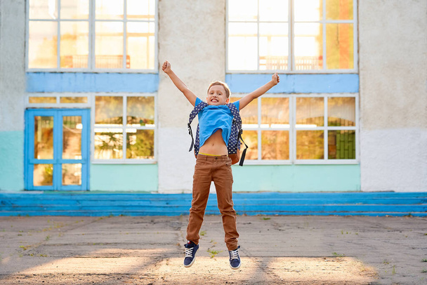 Happy excited schoolboy is happy about end of school year. boy with school bag, jumping for joy against background of school building. child is happy to start holidays. The concept of education - Fotografie, Obrázek