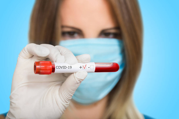 Nurse doctor in medical mask holding test tube with positive coronavirus test blood sample on blured background - Photo, Image