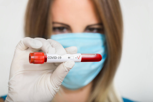 Sestra lékař v lékařské masce držení zkumavky s negativní koronavirus test vzorek krve na modrém pozadí - Fotografie, Obrázek