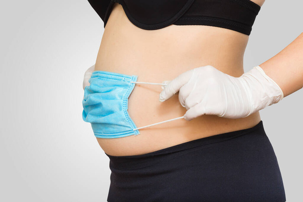 Covid19 e gravidez. Colocando máscara médica protetora na barriga das mulheres fechar em fundo cinza
 - Foto, Imagem