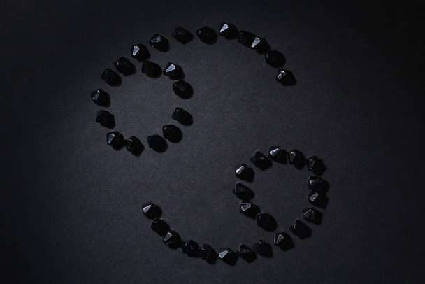Symbol of the zodiac sign Cancer made by black stones on a black background. Low dark key. Vignetting lighting. Horoscope Theme - Photo, Image
