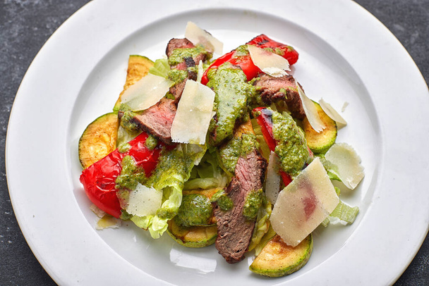 Salade chaude avec veau, légumes cuits au four, poivron, courgettes et parmesan, sur une assiette blanche, sur fond sombre
 - Photo, image