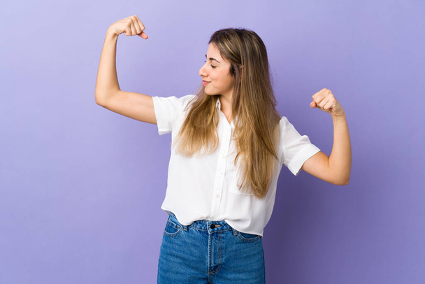Young woman over isolated purple background doing strong gesture - Foto, imagen