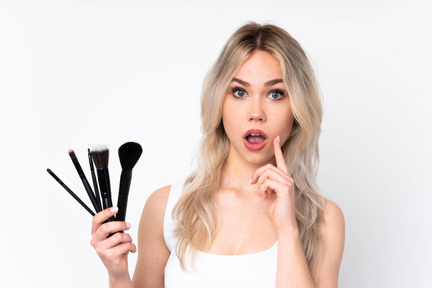Teenager blonde girl over isolated white background holding makeup brush - Fotó, kép