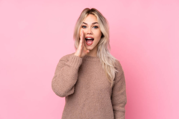 Teenager blonde Mädchen trägt einen Pullover über isoliertem rosa Hintergrund schreit mit weit geöffnetem Mund - Foto, Bild