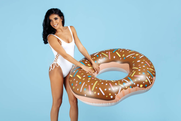 Stylish fit young woman dressed in swimsuit posing happy with donut inflatable circle over blue background. - Fotografie, Obrázek