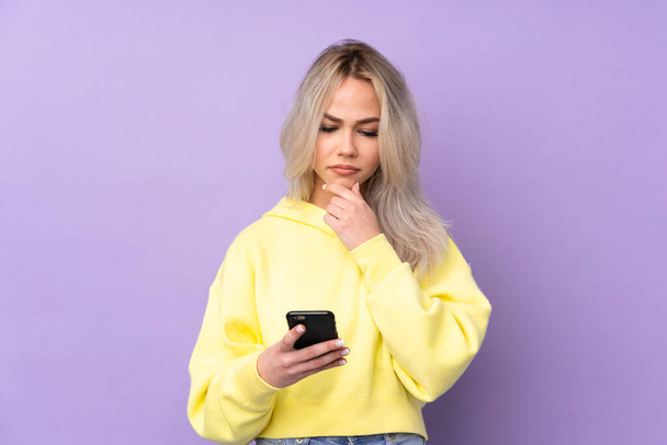 Adolescente portant un sweat-shirt jaune sur fond violet isolé pensant et envoyant un message
 - Photo, image