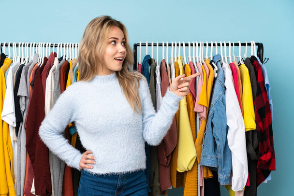 Подростковая русская девушка покупает одежду на синем фоне, указывая пальцем в сторону и представляя продукт
 - Фото, изображение