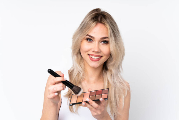 Teenager blonde girl over isolated white background with makeup palette and happy - Photo, Image