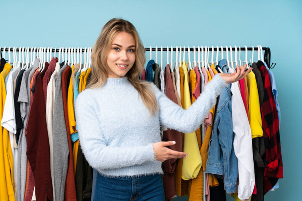 Teenager Russian girl buying some clothes isolated on blue background extending hands to the side for inviting to come - Photo, Image