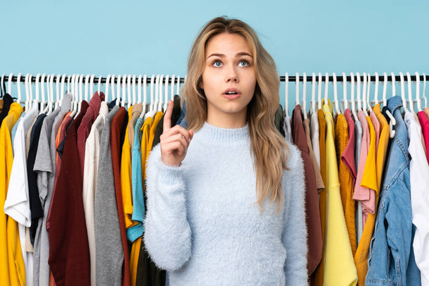 Teenager rusky dívka kupovat nějaké oblečení izolované na modrém pozadí myšlení nápad ukazující prstem nahoru - Fotografie, Obrázek