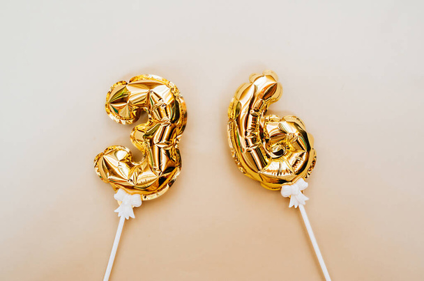 kleine folie gouden ballonnen nummers 36 opgeblazen met helium op een witte stok op een beige delicate achtergrond. glinsterende vakantie begroeting lay-out - Foto, afbeelding