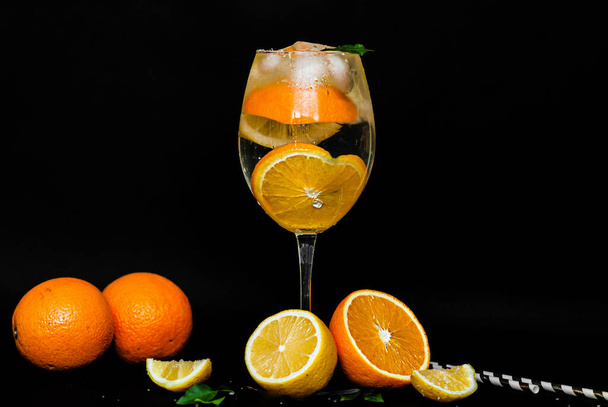 vidro transparente com um coquetel cítrico. Gotas de água e condensado fluem para baixo de um copo com uma bebida com laranjas, limão, gelo e hortelã em um fundo preto. Imagem para menu, conteúdo de barra
 - Foto, Imagem