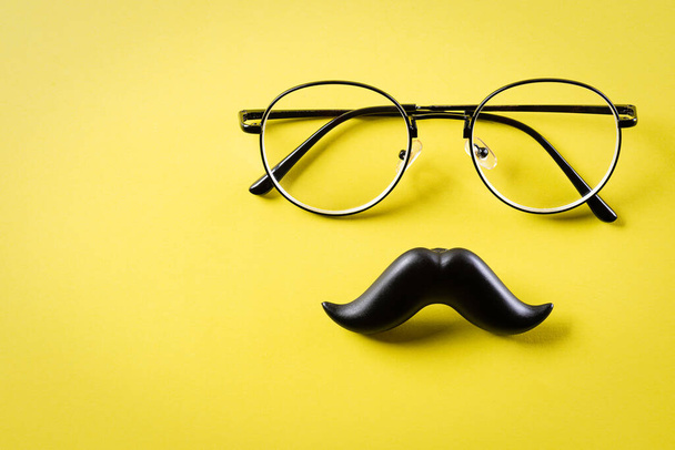 Vatertagskonzept. Schwarzer Schnurrbart und Brille auf gelbem Papierhintergrund. - Foto, Bild
