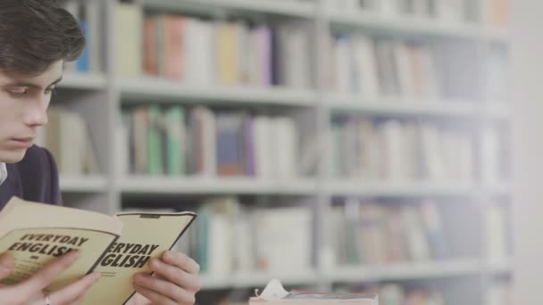 Een jonge student studeert hard in de bibliotheek. Mannelijke student doet studie onderzoek in de bibliotheek met boeken - Video