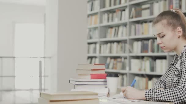 cyoung estudante do sexo feminino escrever em seus livros didáticos na biblioteca
 - Filmagem, Vídeo