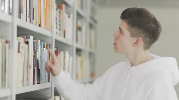 Mann sucht Buch im Bücherregal der Bibliothek am College - Filmmaterial, Video