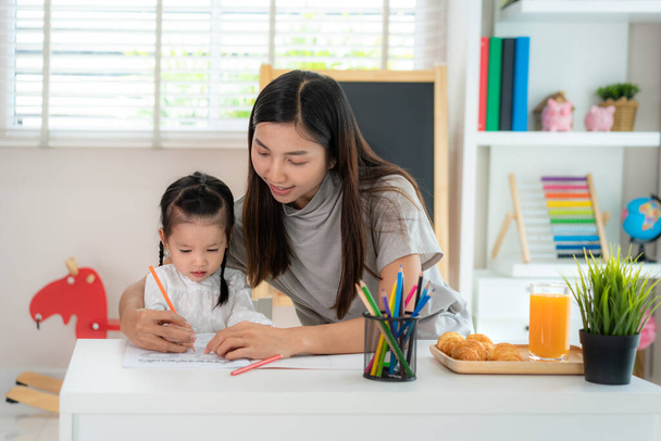 Asian kindergarten student girl with mother painting picture in book with color pencil at home, Homeschooling and distance learning - Foto, immagini