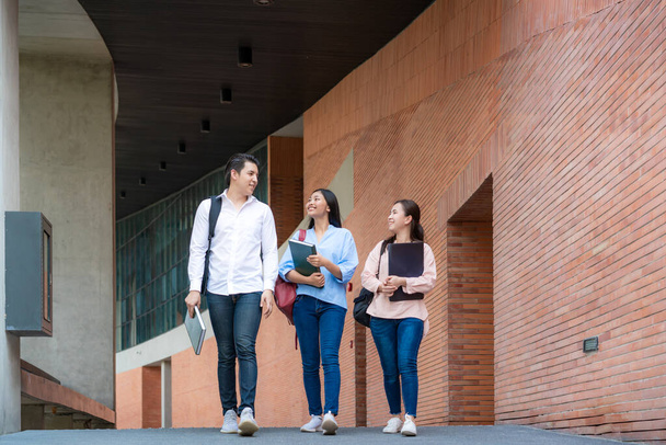 Asiatico tre studenti stanno camminando e parlando insieme nella sala universitaria durante la pausa in Università. Educazione, Istruzione, Studente, Campus, Università, Stile di vita - Foto, immagini
