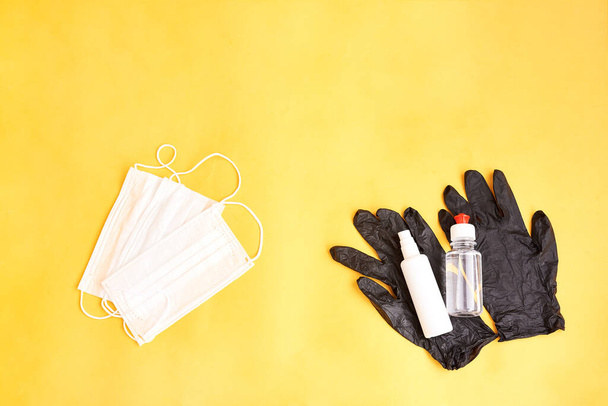 Medical protective mask and antiseptic bottles on black gloves isolated on yellow background. Healthcare medical Coronavirus quarantine - Foto, Imagem