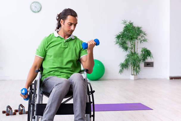 Jongeman in een rolstoel die binnen oefeningen doet - Foto, afbeelding