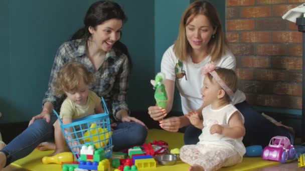 Malé holčičky a jejich maminky si hrají s barevnými plastovými cihlami - Záběry, video