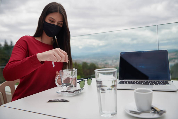 woman sitting separated in restaurant drinking tea wearing medical protective face to protect infection from coronavirus covid-19, restaurant and social distancing concept - Foto, afbeelding