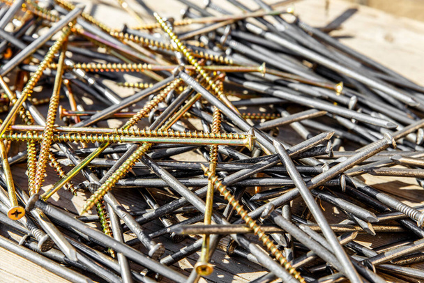 Iron nails and screws on a wooden background. Long, metal, carpenters nails and self-tapping screws for construction. Fixing tool. The view from the top. - 写真・画像