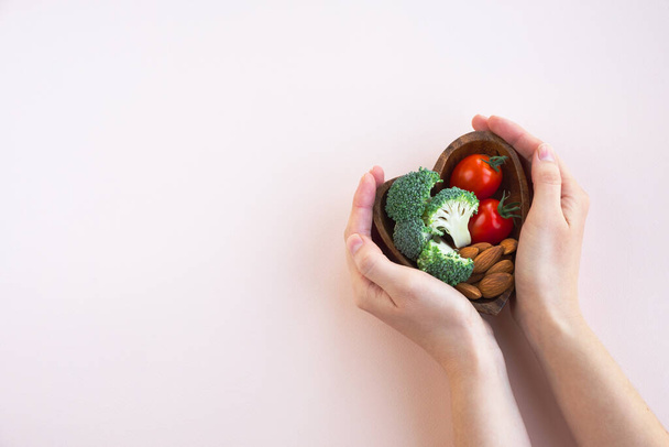 Egészséges étel a szívnek, könnyű háttérrel. Egy tányér zöldségekkel és mogyorókkal egy nő kezében. Táplálkozás és orvostudomány. Felülnézet, másolás - Fotó, kép