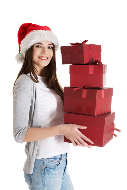 Young beautiful woman in santa hat, holding stock of presents. - 写真・画像