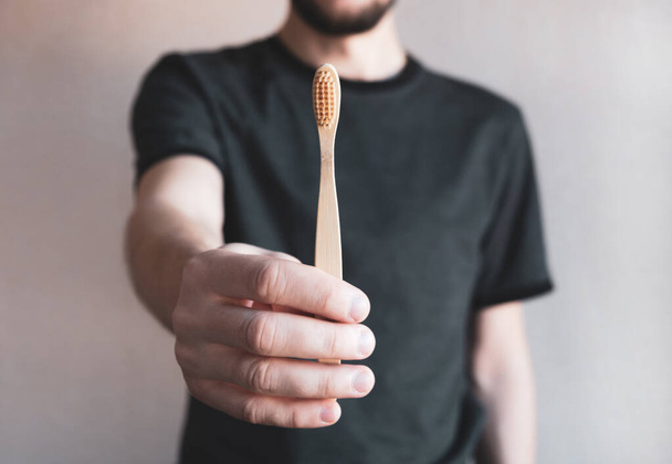 Hombre sosteniendo un cepillo de dientes de bambú sobre un fondo claro. Cero desperdicio, concepto de estilo de vida ecológico y saludable. De cerca.
 - Foto, Imagen
