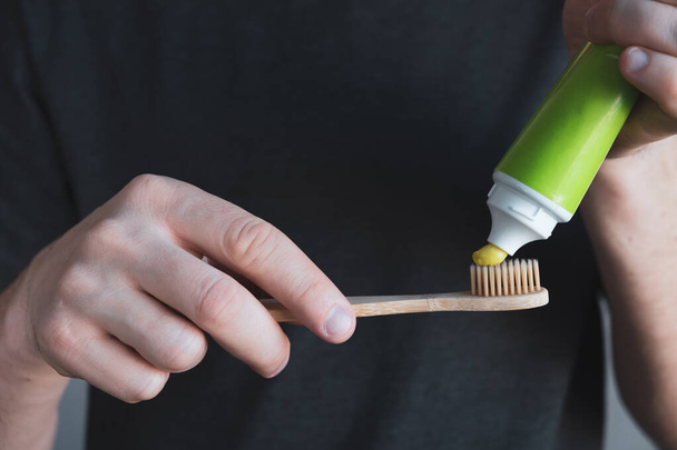Man hands hold green toothpaste and bamboo toothbrush. Dental hygiene and oral care concept. Close up - Foto, Imagen