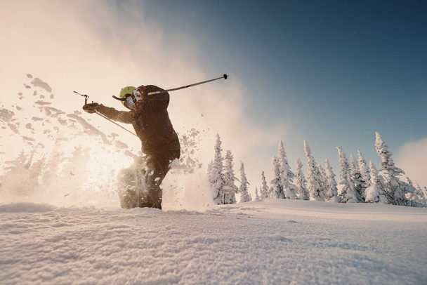 Happy Skier skiing and jump in mountains against sunshine on fresh snow powder between snow-covered spruce forest. Sunny winter day and free ride in ski-resor - Foto, Imagem