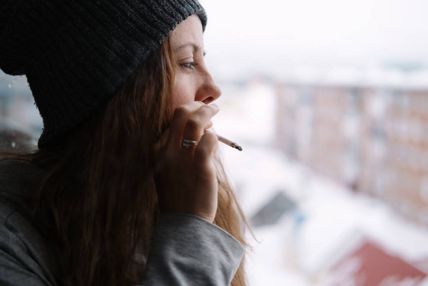 Female wearing hat smoking self-roll weed cigarette blowing smoke - Foto, imagen