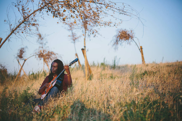 Portrait of musician African man  wearing dreadlocks holding guitar outdoor - Foto, Imagen