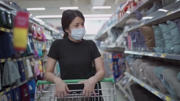Ağır çekimde çalışan Asyalı kadın Covid-19 salgını sırasında süpermarkette market arabası iterken maske takıyor. Genç bayan malzeme stokluyor, karantina karşıtı ve sosyal mesafeler, siyah gömlek, sosyal güvenlik - Video, Çekim