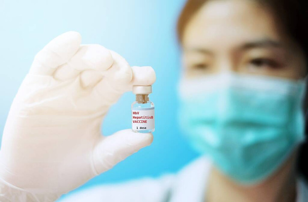 Médica asiática com máscara cirúrgica e luvas de borracha branca em uma clínica, segurando um frasco de vidro de 1 dose de vacina HBV com fundo branco e letras vermelhas
. - Foto, Imagem