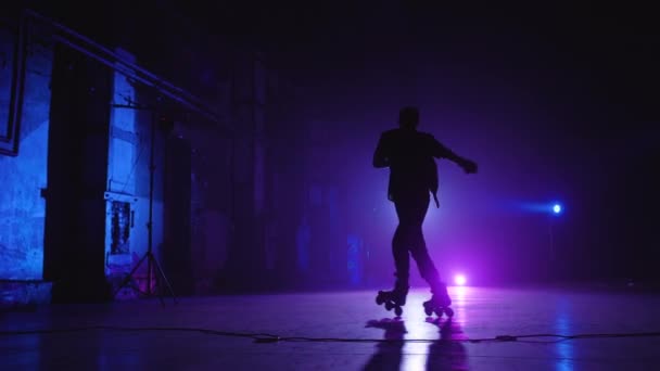 青と紫の照明の下でステージの周りに乗ってキャップやシャツを着て、様々な複雑なトリックやターンを行うプロのローラースケートのリアショット。経験豊富なローラースケートのパフォーマンス - 映像、動画