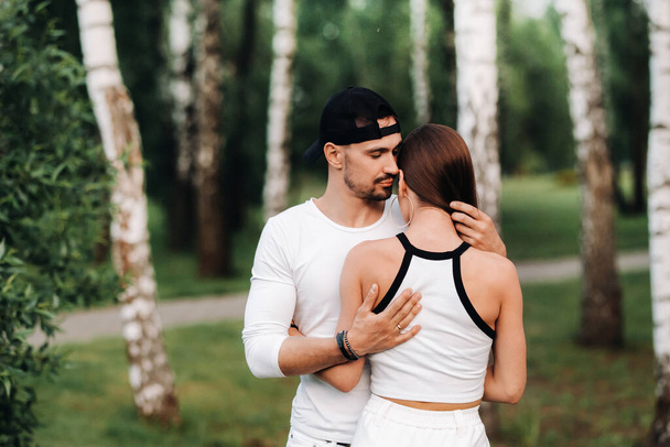 A young beautiful couple in white clothes against the background of a birch grove.Portrait of people in love in a Park in nature - Foto, afbeelding