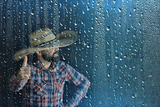 agricultor em um chapéu de palha atrás de gotas de chuva de vidro, américa tempo sazonal oeste selvagem
 - Foto, Imagem