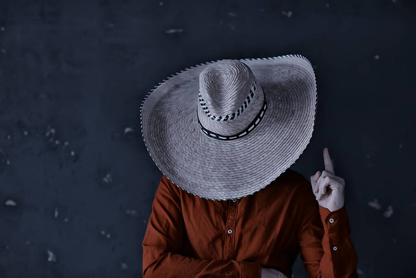 man in a straw hat with brim in the studio gestures with his hands and fingers, points. West america mexico sambrero style - Fotografie, Obrázek
