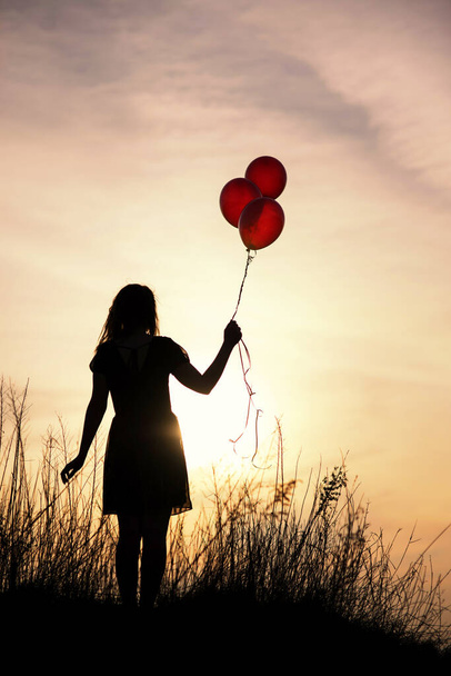 Dziewczyna trzyma balony w dłoni zachód słońca podczas zachodu słońca - Zdjęcie, obraz