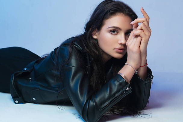 brunette girl in a black leather jacket lies on a blue background - Foto, afbeelding