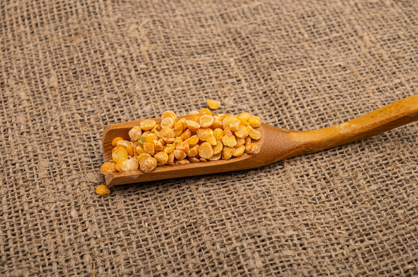 Yellow split peas in a wooden spoon on a background of burlap with a rough texture. Traditional cereals for making soups and porridge. Close up - 写真・画像
