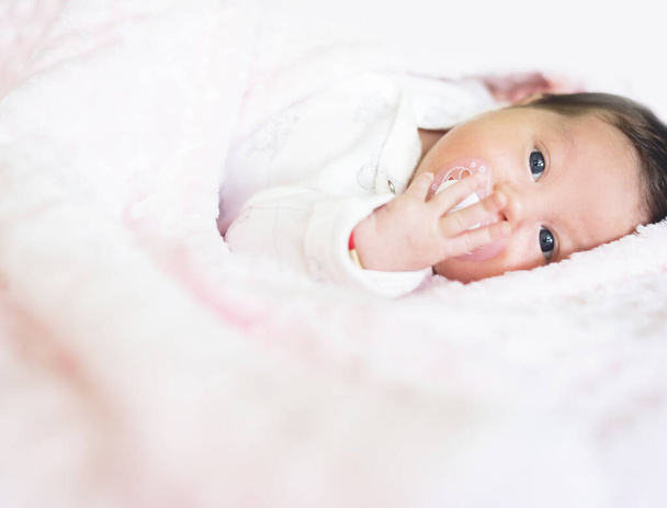 Beau bébé gît enveloppé dans une couverture rose avec un mamelon en plastique dans la bouche. Bébé tenant le mamelon avec de petits doigts, regardant la caméra. Copier l'image papier peint espace
 - Photo, image